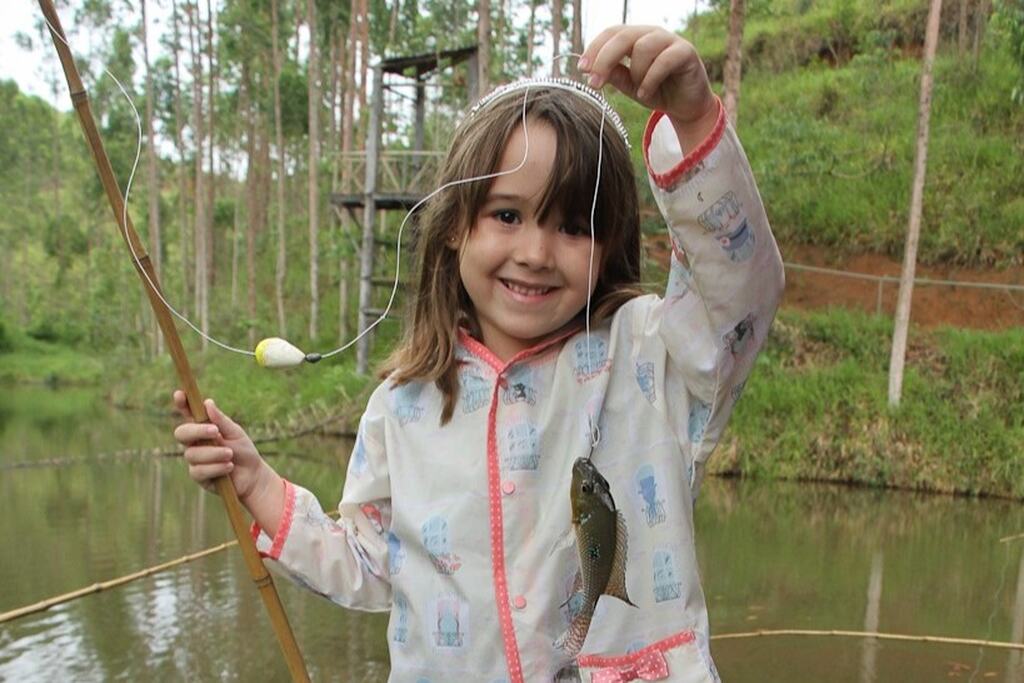 Criança pesca em lago durante atividade ao ar livre em hotel fazenda, com natureza e diversão para a família.