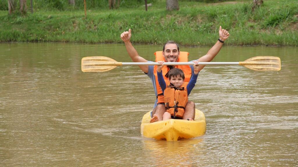 Pai e filho praticam caiaque em lago cercado por natureza durante atividade de lazer em família.