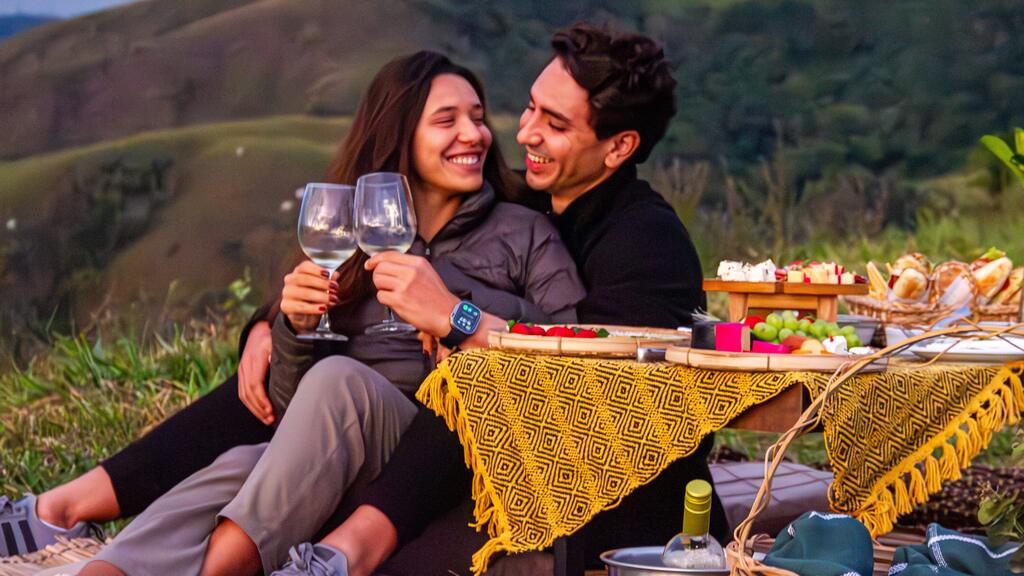 Casal brinda durante um picnic romântico em meio às montanhas e à natureza.